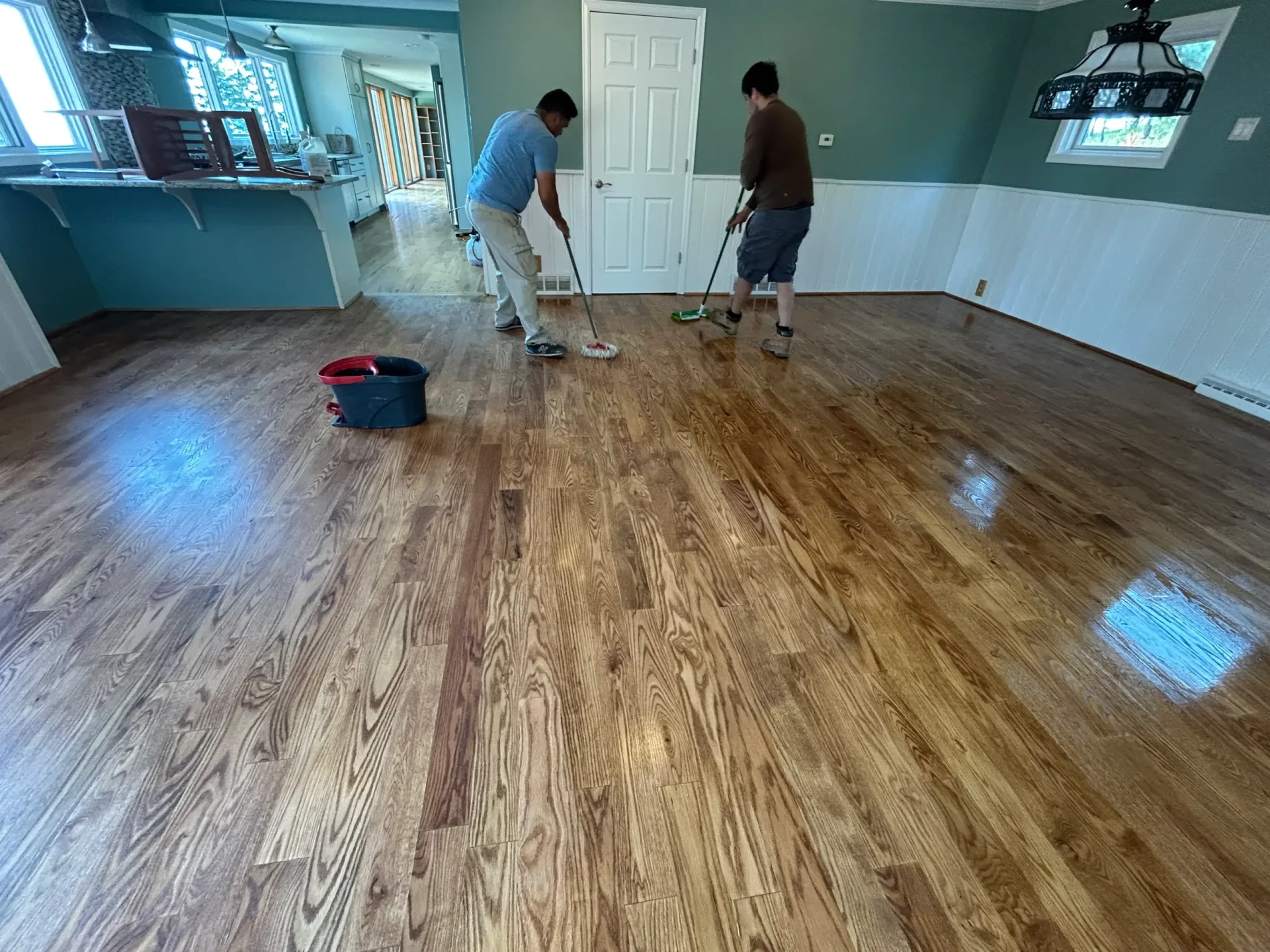 Two crew members applying finish across a floor with applicators