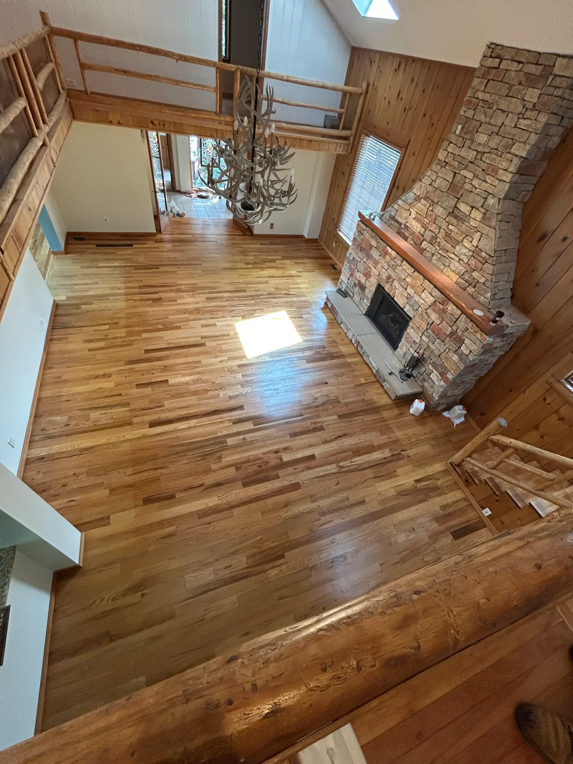 Hardwood floor refinishing under way beside a stone fireplace