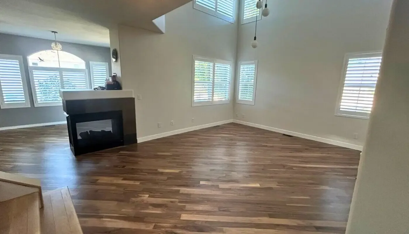 Refinished floor in a double-height great room with a fireplace and shuttered windows