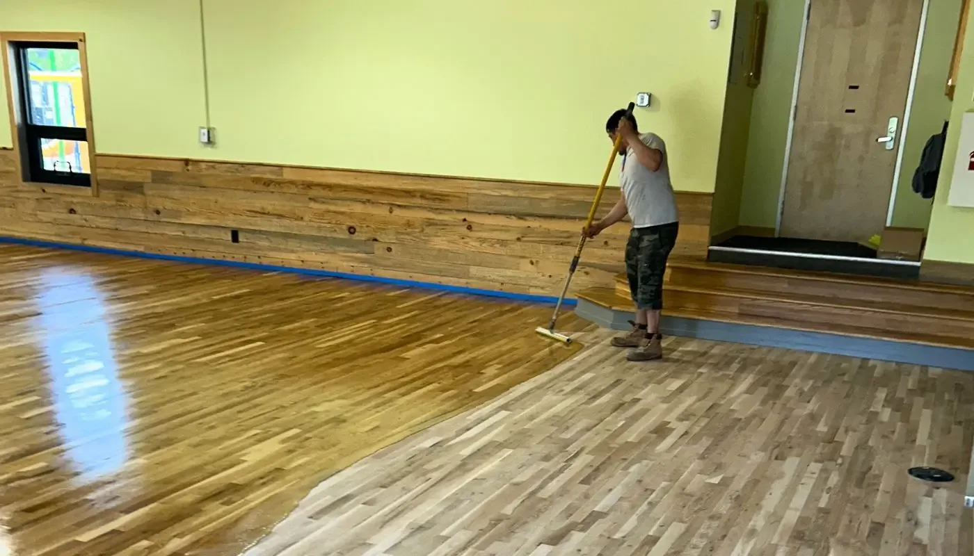 Finish being applied with an applicator across a freshly sanded hardwood floor