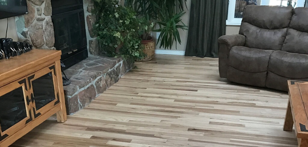 Hardwood flooring in a cozy living room setting with a stone fireplace, wooden furniture, and indoor plants, reflecting modern home design trends in Denver.