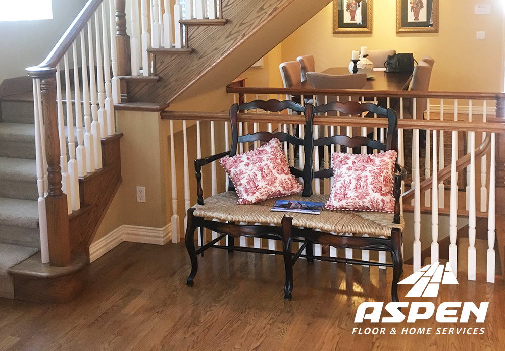 Hardwood staircase and seating area with decorative pillows, showcasing Aspen Floor & Home Services branding, emphasizing quality hardwood flooring in a Denver home.