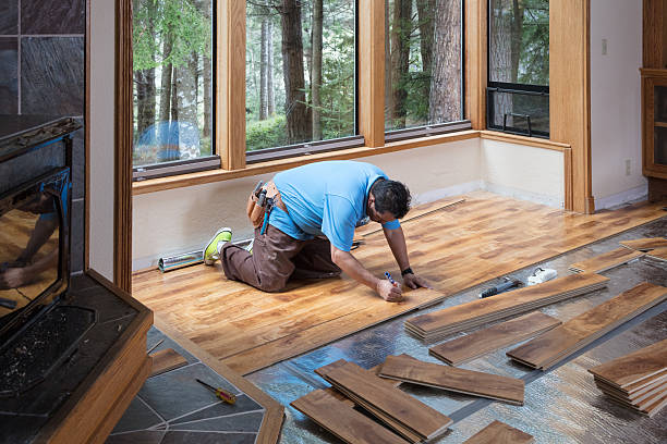 Worker installing wood flooring in a bright room with large windows