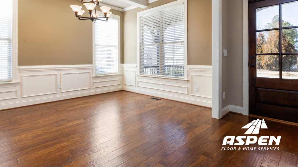 Hardwood floor restoration showcasing polished, rich wood grain in a well-lit room with elegant trim and a chandelier, featuring Aspen Floor & Home Services branding.