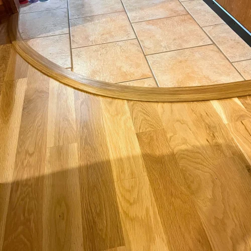 Custom curved hardwood to tile floor transition with precision wood trim installation in Denver home